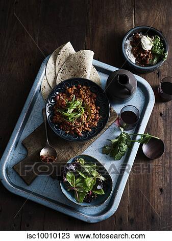 Stock Image - Rustic low key still life with tray of chilli con carne, salad and coffee, overhead view. Fotosearch