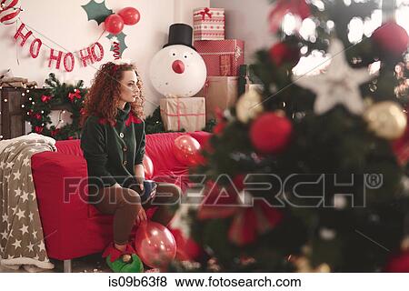 Stock Photo - Sad young woman sitting alone on sofa at christmas. Fotosearch