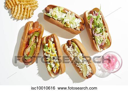 Stock Photograph - Selection of hotdogs with varied garnish and waffle fries, overhead view. Fotosearch
