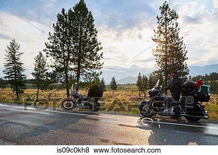Stock Photo - Senior male motorcyclist on rural roadside with motorbike, Dawson Creek, Canada. Fotosearch