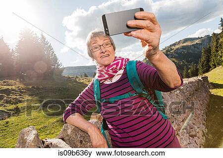 Senior woman, leaning against wall in rural setting, taking selfie, using smartphone, Geneva, Switzerland, Europe View Large Photo Image Stock Photo - Senior woman, leaning against wall in rural setting, taking selfie, using smartphone, Geneva, Switzerland, Europe. Fotosearch