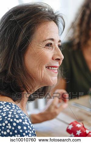 Stock Image - Senior woman listening attentively at dining table. Fotosearch