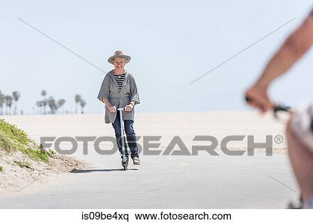 Senior woman riding push scooter on beach View Large Photo Image Stock Photography - Senior woman riding push scooter on beach. Fotosearch
