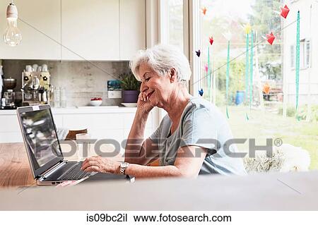 Senior woman sitting at table, using laptop View Large Photo Image Stock Image - Senior woman sitting at table, using laptop. Fotosearch