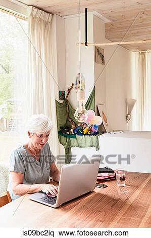 Senior woman sitting at table, using laptop View Large Photo Image Stock Photography - Senior woman sitting at table, using laptop. Fotosearch