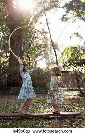 Stock Photograph - Sisters playing with hula hoop in shaded garden. Fotosearch