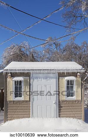 Stock Photo - Storage shed facade and overhead electrical wires covered in icicles and snow in residential backyard after ice storm in early spring, Quebec, Canada. Fotosearch