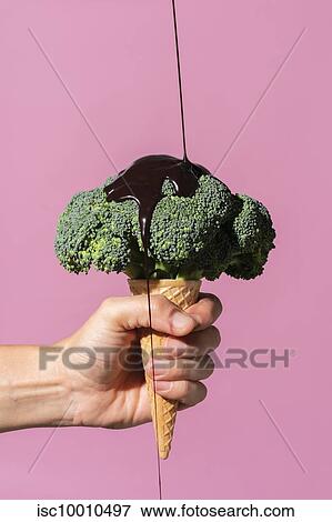 Studio shot of man's hand holding ice cream cone with broccoli on top and pouring chocolate sauce, against pink background View Large Photo Image Stock Photo - Studio shot of man's hand holding ice cream cone with broccoli on top and pouring chocolate sauce, against pink background. Fotosearch