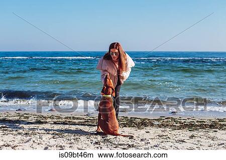 Picture - Stylish mid adult woman on beach petting her dog, Odessa, Odeska Oblast, Ukraine. Fotosearch