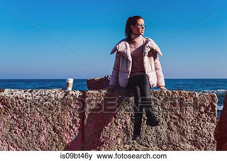 Stock Photo - Stylish mid adult woman sitting on sea wall, Odessa, Odeska Oblast, Ukraine. Fotosearch