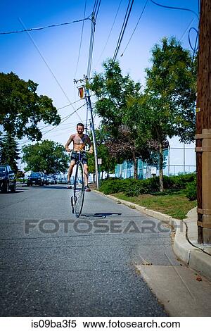 Tattooed young man cycling suburban road on penny farthing View Large Photo Image Stock Photography - Tattooed young man cycling suburban road on penny farthing. Fotosearch