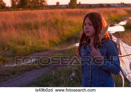 Stock Image - Teenage girl carrying kite over her shoulder along dirt track at sunset. Fotosearch