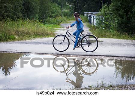 Teenage girl cycling along rural road past puddle View Large Photo Image Picture - Teenage girl cycling along rural road past puddle. Fotosearch