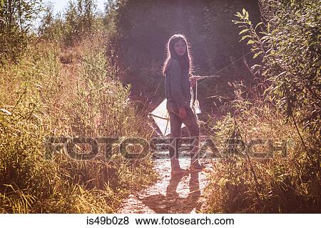 Stock Photo - Teenage girl holding kite looking back from dirt track. Fotosearch