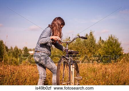 Teenage girl leaning mounting her bicycle in field View Large Photo Image Stock Image - Teenage girl leaning mounting her bicycle in field. Fotosearch