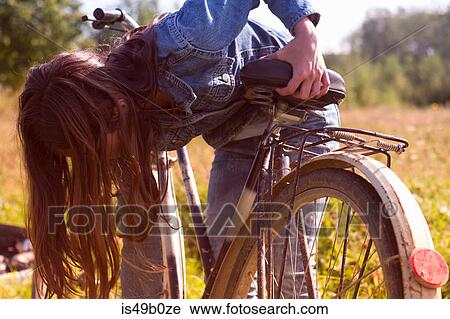 Stock Image - Teenage girl leaning over her bicycle in field. Fotosearch