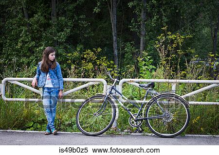 Stock Photography - Teenage girl looking at her bicycle on rural road. Fotosearch