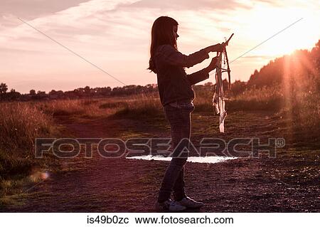 Stock Image - Teenage girl preparing kite on dirt track at sunset. Fotosearch