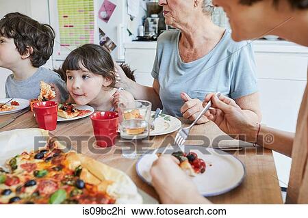Three generation family sitting at kitchen table eating pizza View Large Photo Image Stock Image - Three generation family sitting at kitchen table eating pizza. Fotosearch