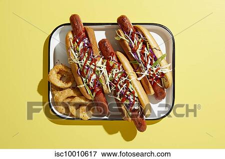Stock Photo - Three hotdogs on tray with onion rings, overhead view on yellow background. Fotosearch