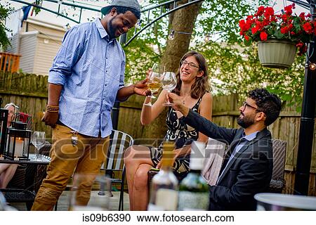 Stock Image - Three people at garden party, holding wine glasses, making a toast. Fotosearch