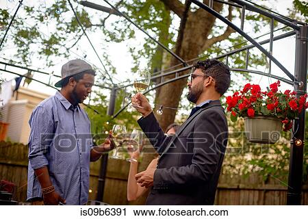 Stock Image - Three people at garden party, holding wine glasses, inspecting wine. Fotosearch