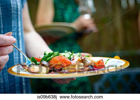 Stock Image - Three people at garden party, sitting, in conversation, holding wine glasses. Fotosearch