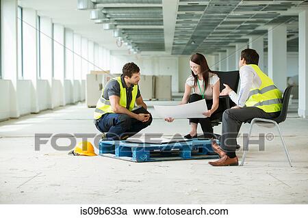Three people sitting in newly constructed office space, looking at construction plans View Large Photo Image Stock Image - Three people sitting in newly constructed office space, looking at construction plans. Fotosearch