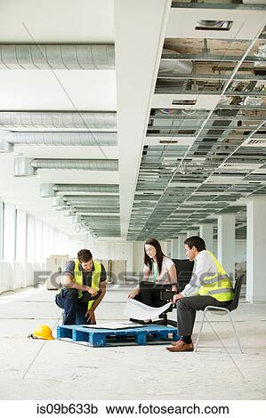 Stock Image - Three people sitting in newly constructed office space, looking at construction plans. Fotosearch