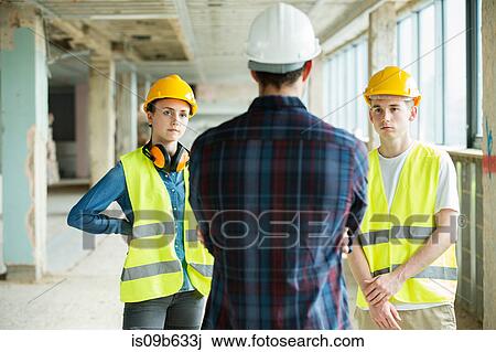 Three people standing in constructions site, wearing hard hats, having discussion View Large Photo Image Stock Image - Three people standing in constructions site, wearing hard hats, having discussion. Fotosearch