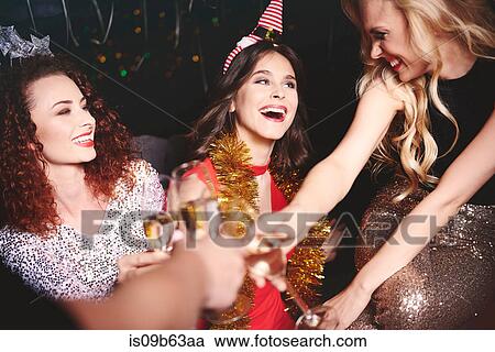 Stock Image - Three women sitting together at party, holding champagne glasses, making a toast. Fotosearch