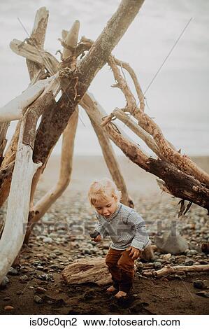 Stock Image - Toddler playing beside wickiup on beach. Fotosearch