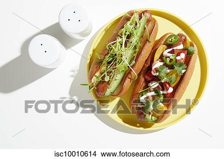 Picture - Two garnished hotdogs on yellow plate, overhead still life. Fotosearch