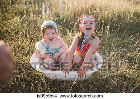 Two girls in field, playing in plastic tub of water View Large Photo Image Picture - Two girls in field, playing in plastic tub of water. Fotosearch
