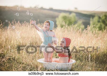 Two girls in field, playing in plastic tub of water View Large Photo Image Stock Image - Two girls in field, playing in plastic tub of water. Fotosearch