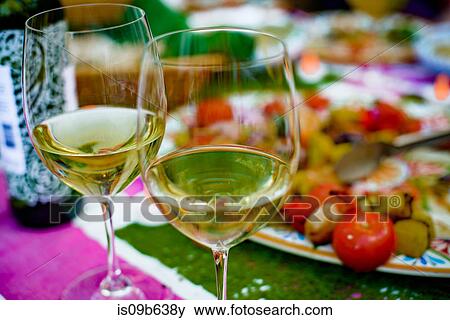 Stock Photo - Two half filled wine glasses on table, food on plate behind, close-up. Fotosearch