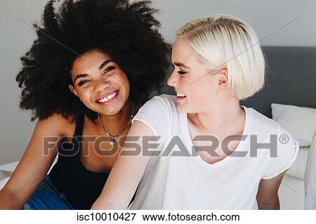 Two happy young female friends sitting on bed, portrait View Large Photo Image Stock Photo - Two happy young female friends sitting on bed, portrait. Fotosearch