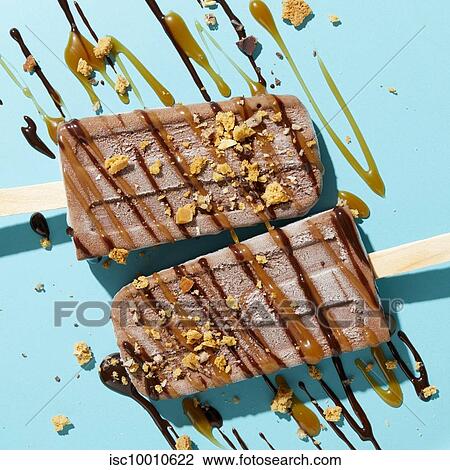 Two homemade fudge iced lollies with sprinkled and drizzled nuts, caramel and chocolate sauce on blue background, overhead view View Large Photo Image Stock Image - Two homemade fudge iced lollies with sprinkled and drizzled nuts, caramel and chocolate sauce on blue background, overhead view. Fotosearch