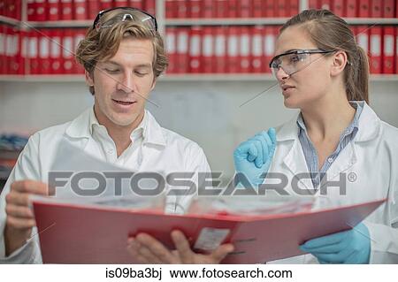 Stock Image - Two lab workers, looking at folder of paperwork. Fotosearch
