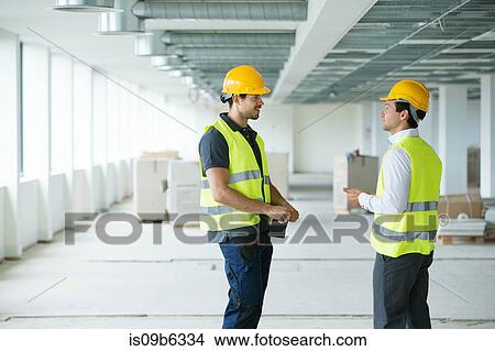 Two men wearing hi vis vest, having discussion in newly constructed office space View Large Photo Image Picture - Two men wearing hi vis vest, having discussion in newly constructed office space. Fotosearch
