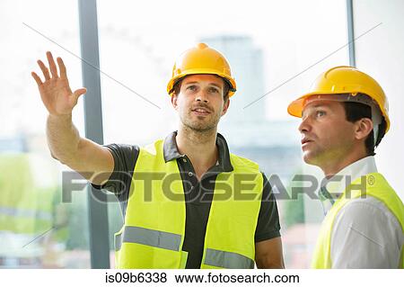 Stock Photo - Two men wearing hi vis vest, having discussion in newly constructed office space. Fotosearch