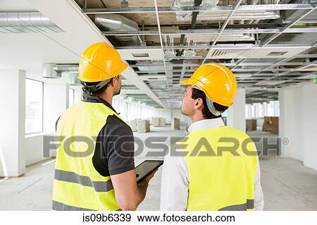 Two men wearing hi vis vest, having discussion in newly constructed office space, rear view View Large Photo Image Stock Photo - Two men wearing hi vis vest, having discussion in newly constructed office space, rear view. Fotosearch