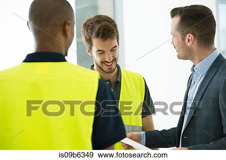 Two men wearing hi vis vests, having discussion with businessman View Large Photo Image Stock Photo - Two men wearing hi vis vests, having discussion with businessman. Fotosearch