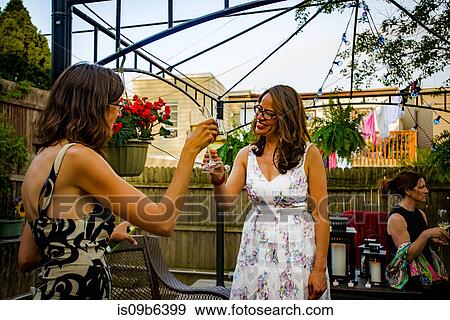 Two women at garden party, holding wine glasses, making a toast View Large Photo Image Stock Photo - Two women at garden party, holding wine glasses, making a toast. Fotosearch