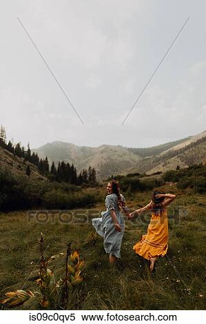 Stock Photography - Two women holding hands running in rural valley, rear view, Mineral King, California, USA. Fotosearch