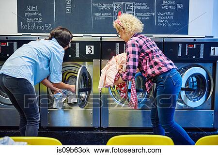 Two women inserting laundry into washing machines at laundrette View Large Photo Image Stock Image - Two women inserting laundry into washing machines at laundrette. Fotosearch