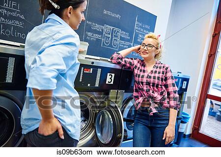 Two women talking by washing machines at laundrette View Large Photo Image Picture - Two women talking by washing machines at laundrette. Fotosearch