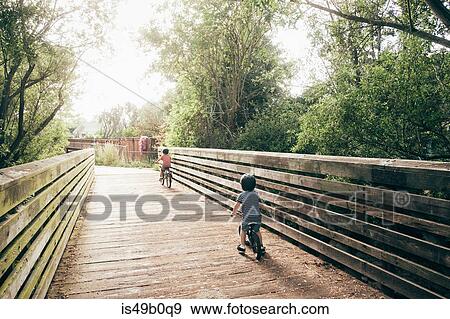 Two young boys riding bicycles across bridge, rear view View Large Photo Image Stock Photo - Two young boys riding bicycles across bridge, rear view. Fotosearch