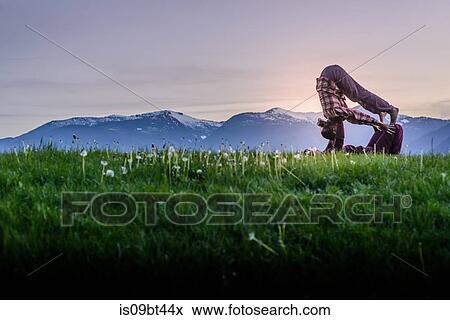 Two young women 0acticing acroyoga on grass in front of mountain range at sunset, Squamish, British Columbia, Canada View Large Photo Image Stock Photo - Two young women 0acticing acroyoga on grass in front of mountain range at sunset, Squamish, British Columbia, Canada. Fotosearch