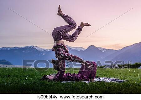 Two young women 0acticing acroyoga on grass in front of mountain range at sunset, Squamish, British Columbia, Canada View Large Photo Image Stock Photo - Two young women 0acticing acroyoga on grass in front of mountain range at sunset, Squamish, British Columbia, Canada. Fotosearch